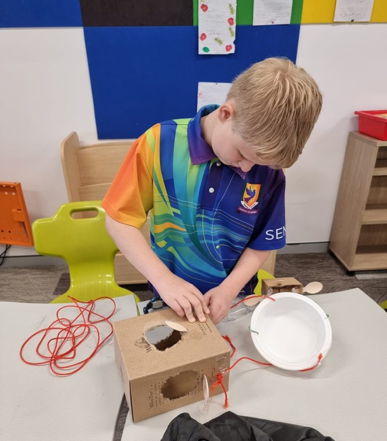 A Radiant Life College student in the school uniform, focused on assembling a cardboard structure with string and a bowl.